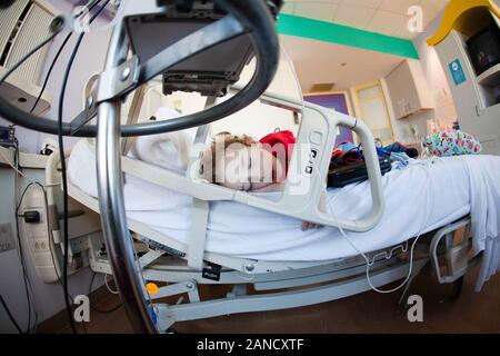 Lockiges Kleinkind schläft allein im großen Krankenhausbett. Stockfoto