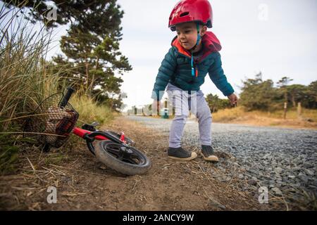 Kleinkind Junge lehnt sich rüber, um Fahrrad zu holen. Stockfoto