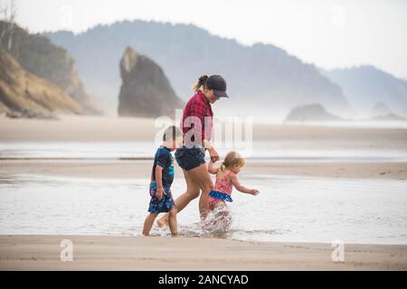 Seitenansicht der Mutter, die mit ihren beiden kleinen Kindern am Strand spazieren ging. Stockfoto