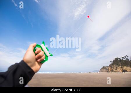 Menschliche Hand hält sich am Strand an den roten Drachen. Stockfoto