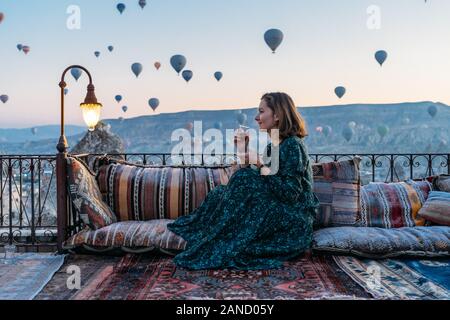 Frau trinkt früh Morgen Tee mit Heißluftballons in Kappadokien Stockfoto