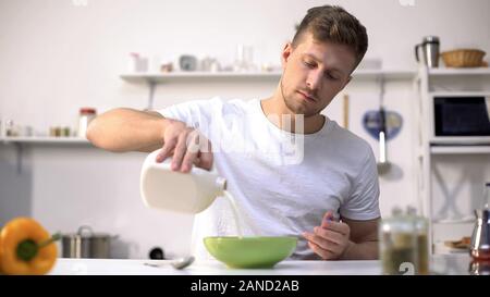 Männliche gießen Milch in Schüssel mit Corn Flakes, nahrhaftes und gesundes Frühstück Stockfoto