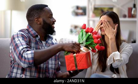Schwarzer Mann präsentiert Tulpen und Geschenk, um seine Freundin, urlaub Feier Stockfoto