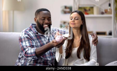 Multiethnischen Familie Schmusen auf dem Sofa, Frau Münzen im Sparschwein, Einsparungen Stockfoto