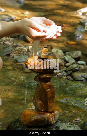 Junge Frau gießt Wasser über einen Felsen Turm durch den Fluss Stockfoto