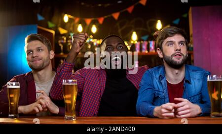 Afro-amerikanischer Mann feiern ihre Mannschaft zum Sieg, kaukasische Freunde umgekippt Stockfoto