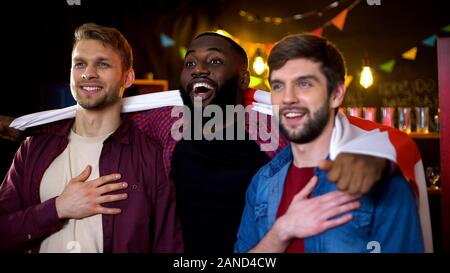 Lächelnd multiethnischen Freunde in englischer Flagge umarmen gewickelt, Sport Stockfoto