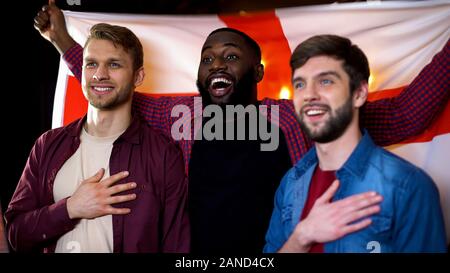Weißen und Schwarzen männlichen Freunde singen Nationalhymne, winken englische Flagge Stockfoto