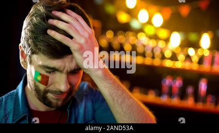 Nervös portugiesischen Fußball-Fan mit Fahne auf der Wange halten Kopf, Team zu verlieren. Stockfoto