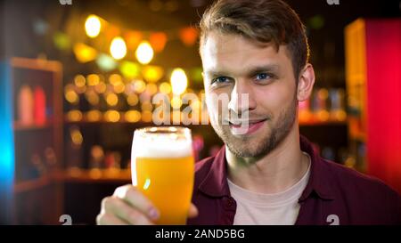 Stattliche Mann hält ein Glas frisches Bier, Ausgabe Zeit an die Brauerei, Bierverkostung Stockfoto