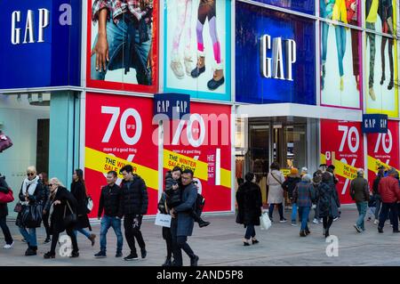 London Shoppers Oxford Street London Einzelhandelseinkäufer Menschen, die am Kaufhaus GAP vorbeilaufen farbenfrohe Geschäfte mit 70 % Rabatt, wie im Januar 2020 in der Oxford Street, London, Großbritannien Stockfoto