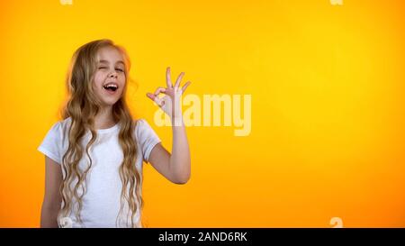 Hübsche Blondine jugendlich Mädchen mit lockigem Haar, ok Zeichen und winking, Vorlage Stockfoto