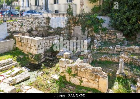 Eine orange und weiße Katze entspannt auf einem Stein in einem unterirdischen Bereich voll von antiken Ruinen im Plaka Viertel von Athen, Griechenland. Stockfoto