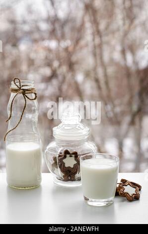 Glas voll Milch, Schokolade, Kekse und eine Flasche am Frühstückstisch auf wintwr Fenster anzeigen. Stockfoto