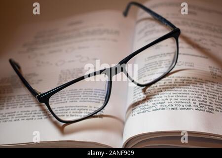 Lesebrille auf einem geöffneten Buch, mit schönen Schatten fallen auf die Wörter. Stockfoto