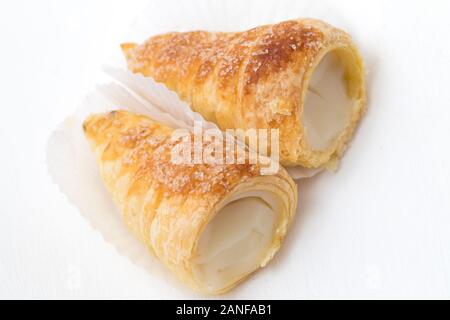 Blätterteig Horn mit Weiß Creme oder vla Susu auf einem weißen Hintergrund. Puff Horn mit Weiß Creme auf einem Spiegel Hintergrund gefüllt, close-up. Stockfoto