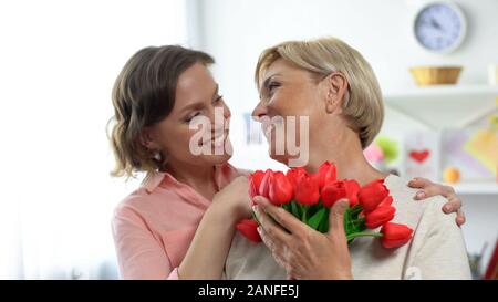 Lächelnd Tochter umarmen ältere Mutter, holding Tulpen Geschenk, Urlaubsgrüße Stockfoto