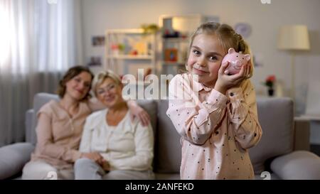 Tochter holding Sparschwein, Mutter und Oma hinter, Lehre, um Geld zu sparen Stockfoto