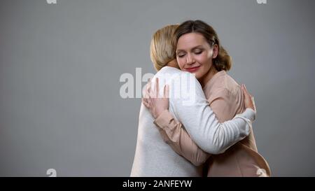 Junge weibliche Umarmen ältere Mutter auf grauem Hintergrund, Familie, Liebe Stockfoto