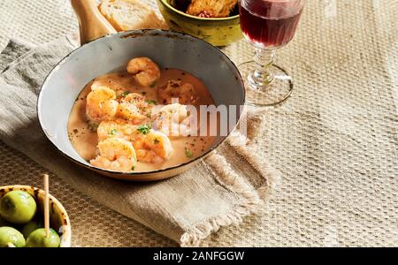 Scampi Hummer mit Käse sahne Soße in alten Pan auf rustikalen Tisch mit Oliven, Brot und Rotwein. Traditionelle spanische Küche studio Shot mit Stockfoto