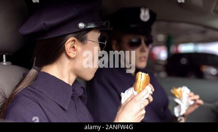 Beamtinnen der Pflicht zu Mittag essen, essen Burger im Streifenwagen, ungesunde Ernährung Stockfoto