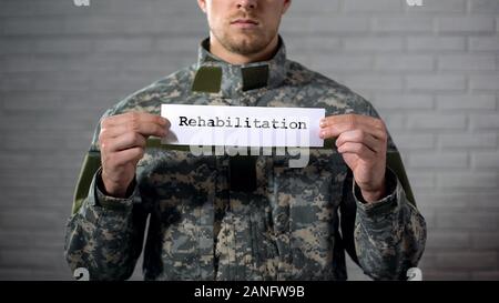 Rehabilitation Wort auf Zeichen in den Händen der männlichen Soldaten geschrieben, Gesundheit Unterstützung Stockfoto