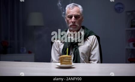 Unglücklich älterer Mann am Kuchen suchen und geblasen Kerze, trauriger Geburtstag, Einsamkeit Stockfoto