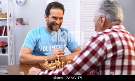 Lächelnde Männer mittleren Alters freiwilligen Schach spielen mit älteren Menschen im Pflegeheim Stockfoto