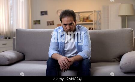 Traurig einsamer Mann aggressiv in Kamera auf dem Sofa zu Hause sitzen suchen, Problem Stockfoto