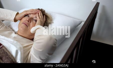 Ältere Frau im Krankenbett holding Kopf, Leiden schreckliche Migräne, Gesundheitswesen Stockfoto
