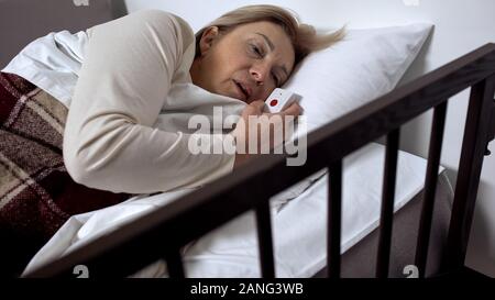 Reife weibliche Patienten liegen im Krankenbett, Unwohlsein und Holding call-Taste Stockfoto