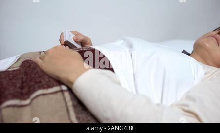 Schwache Frau im Krankenbett drücken der Taste Dosis von Medizin zu nehmen, um die Schmerz zu entlasten Stockfoto