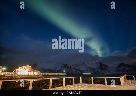 Aurora borealis oder Northern lights über verschneite Berge mit Haus Beleuchtung in Mefjord Brygge, Senja Island, Norwegen Stockfoto