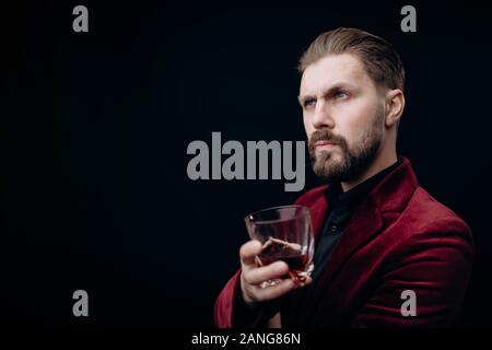 Stattliche viril Männlich in Weinigen Jacke hält ein Glas Branntwein Stockfoto