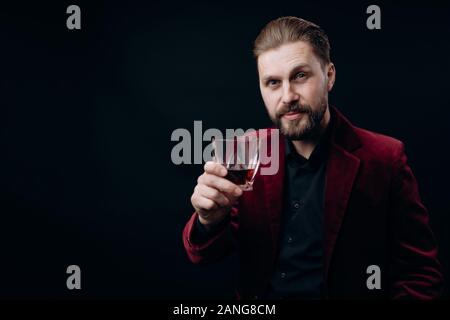 Stilvolle Mann in Weinigen Jacke Toasten mit einem Glas Spirituosen Stockfoto