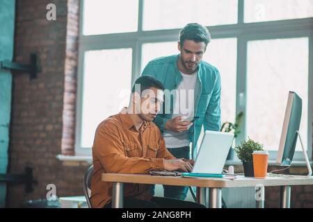 Netter junger Mann in der Nähe von seinem Kollegen stehend Stockfoto