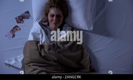 Schreiende Frau mit Wunde im Gesicht im Bett lag, zerrissenes Foto in der Nähe von Kissen, Auflösung Stockfoto