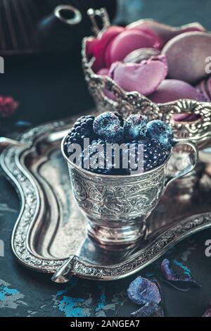 Blau reifen Heidelbeeren und Brombeeren in einem silber Glas auf einem silbernen Tablett auf dem Hintergrund der hausgemachte Teigwaren Cookies. Stockfoto