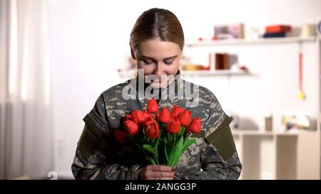 Gerne weibliche Soldaten in Uniform sniffing Aroma der Tulpen Bouquet und lächelnd Stockfoto
