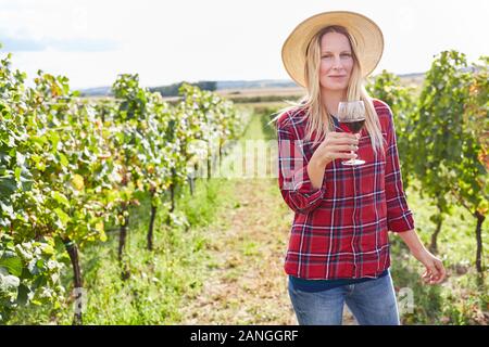 Junge Frau im Weinberg mit einem Glas Rotwein zwischen Reben Stockfoto