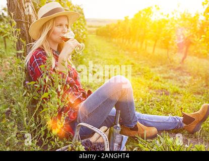 Junge Frau trinkt ein Glas Rotwein mit Picknick im Weinberg im Herbst Stockfoto