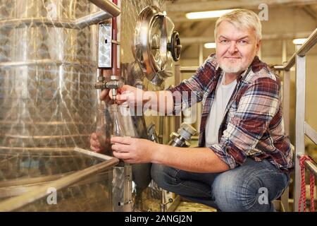 Der Mensch als ein Winzer in einer Weinkellerei prüft, frischen Wein bei der Fermentation Tank Stockfoto