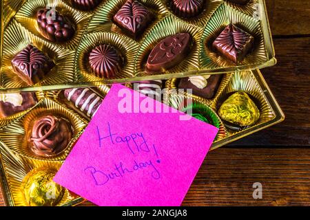 Alles Gute zum Geburtstag text auf Memo post zur Erinnerung, in der Nähe eine goldene Schachtel mit Schokolade Pralinen. Stockfoto