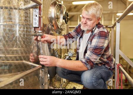 Winzer Kontrollen frische Wein auf der Fermentation Tank in einer Weinkellerei während der Weinbereitung Stockfoto