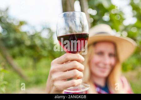 Blonde Frau hält ein Glas Rotwein, während einer Weinprobe im Weinberg Stockfoto