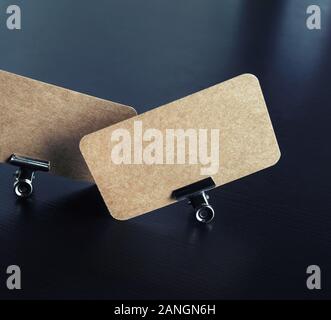 Foto von leeren Kraftpapier Visitenkarten und Metall Binder Clips auf schwarzem Holz Tisch Hintergrund. Stockfoto