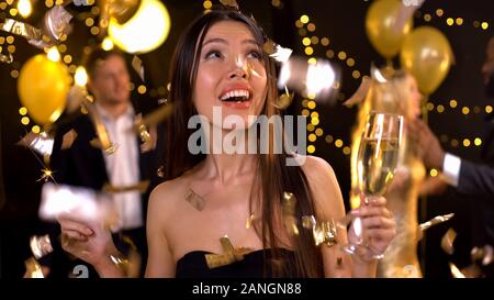 Positive Frau mit Champagner Glas und Wunderkerze, Konfetti fällt. Stockfoto