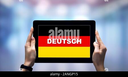 Weibliche Hände, die Tablette mit deutschen Wort gegen die nationale Flagge, online App Stockfoto