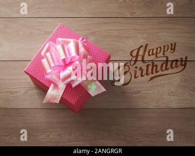 Ein quadratischer Kasten mit pinkfarbenen Punkten und wunderschönem rosa Band auf dem Holztisch und Text im Vintage-Stil zum Happy Birthday Stockfoto