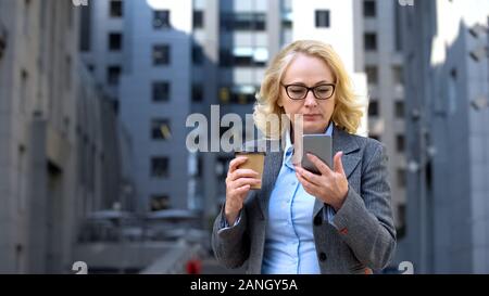 Schwere Leiter der Abteilung lesen Smartphone business news Holding Kaffeetasse Stockfoto